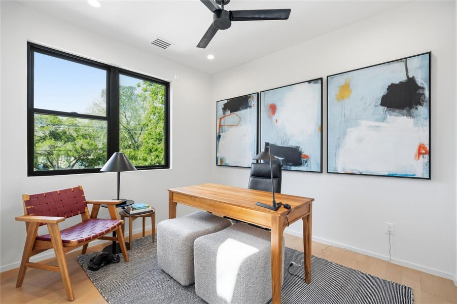 Sun-filled home office features wide-plank wood flooring and generous tree-lined views.