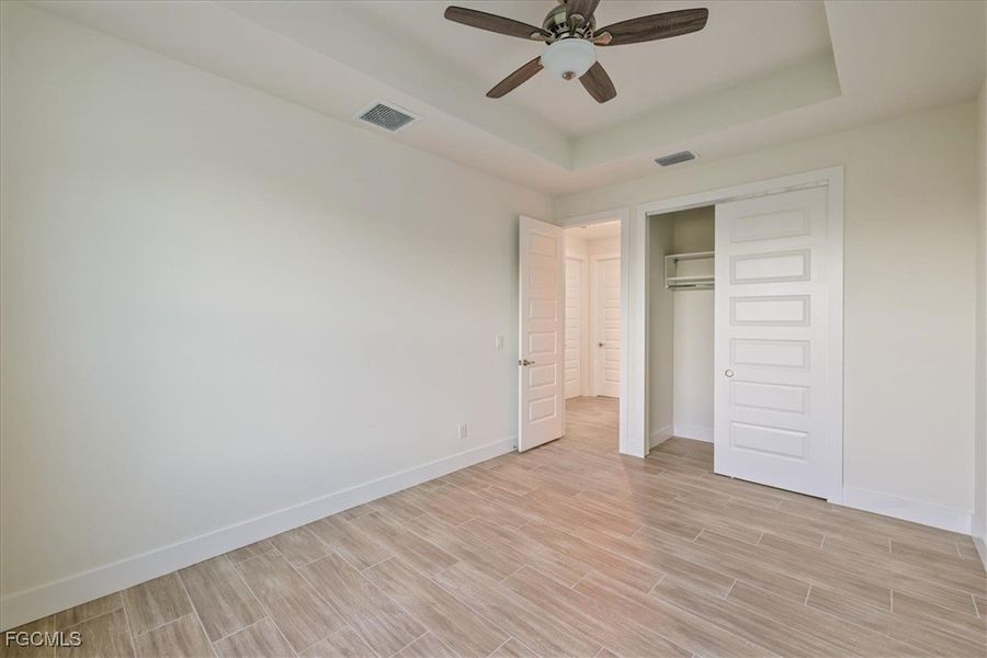 Unfurnished bedroom featuring a raised ceiling, wood finish floors, a closet, and ceiling fan