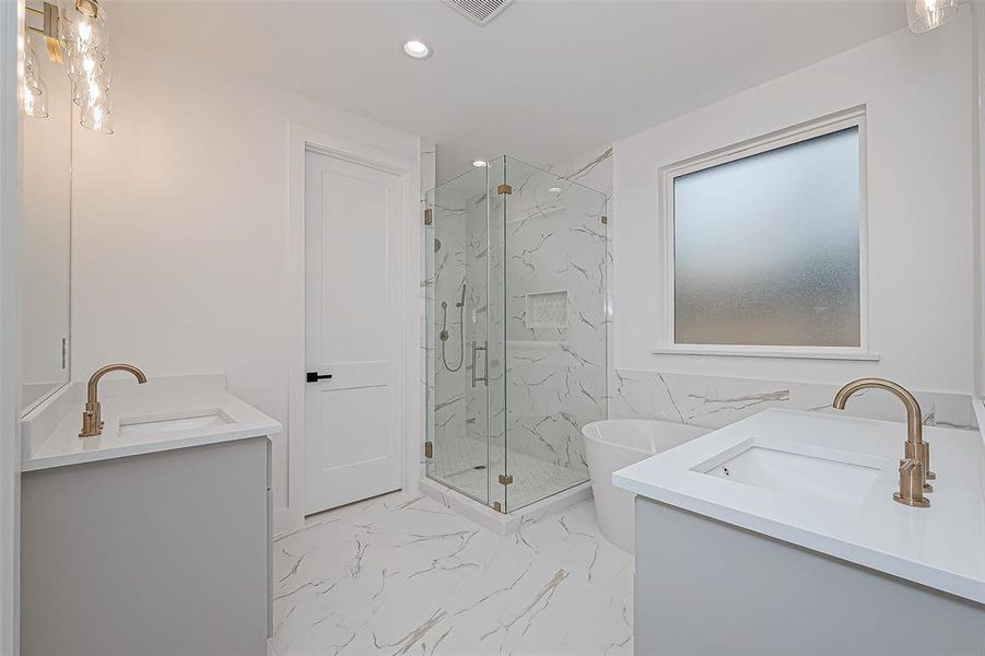 Dual sinks with sleek fixtures, a frameless glass shower, and a freestanding tub. The space is bright, with white marble-style tiles and a frosted window for privacy.