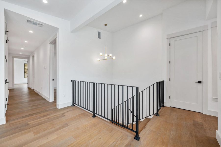 Hall featuring beamed ceiling, light wood finished floors, an upstairs landing, and suspended lighting