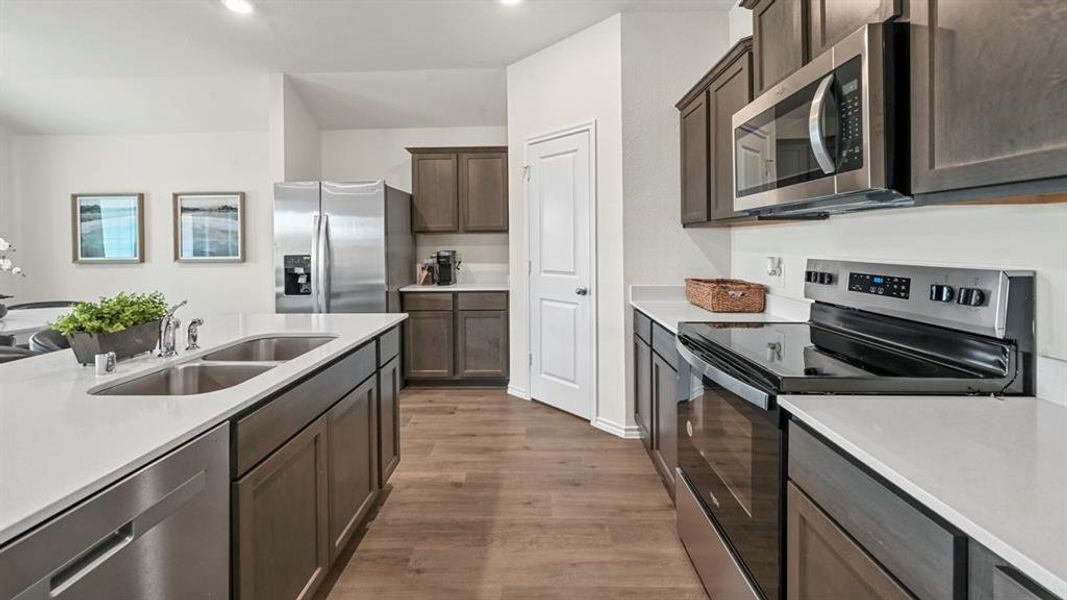 Kitchen with stainless steel appliances, dark wood-type flooring, dark brown cabinetry, and light stone counters Kitchen with stainless steel appliances, dark wood-type flooring, dark brown cabinetry, and light stone counters