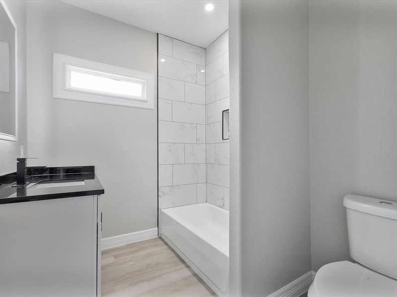 Bathroom with toilet, vanity, wood finished floors, baseboards, and bathtub / shower combination