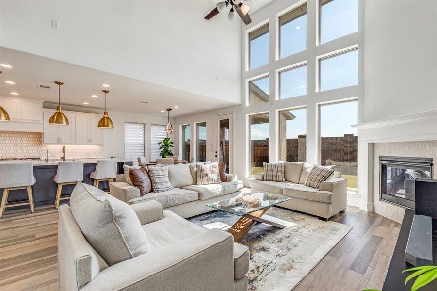 Living room featuring a tile fireplace, ceiling fan, a towering ceiling, light wood finished floors, and recessed lighting