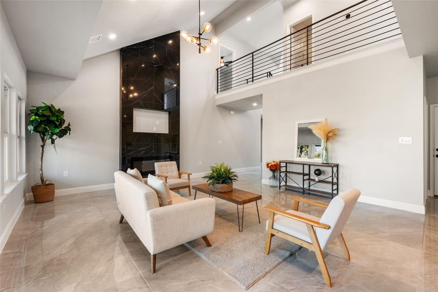 Living room featuring a high end fireplace, high vaulted ceiling, a chandelier, light marble finish flooring, and beamed ceiling