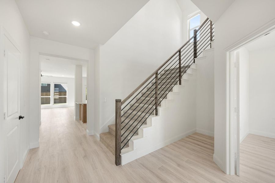 Bright entryway with staircase featuring metal railing, light wood floors, and white walls leading to main living area
