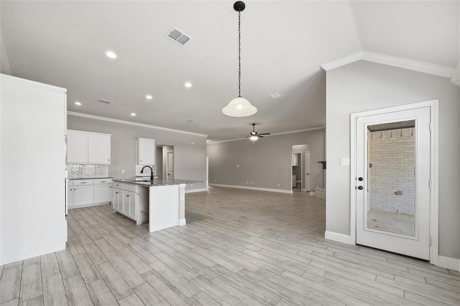 Kitchen with crown molding, a center island with sink, open floor plan, white cabinetry, and hanging light fixtures Kitchen with crown molding, a center island with sink, open floor plan, white cabinetry, and hanging light fixtures