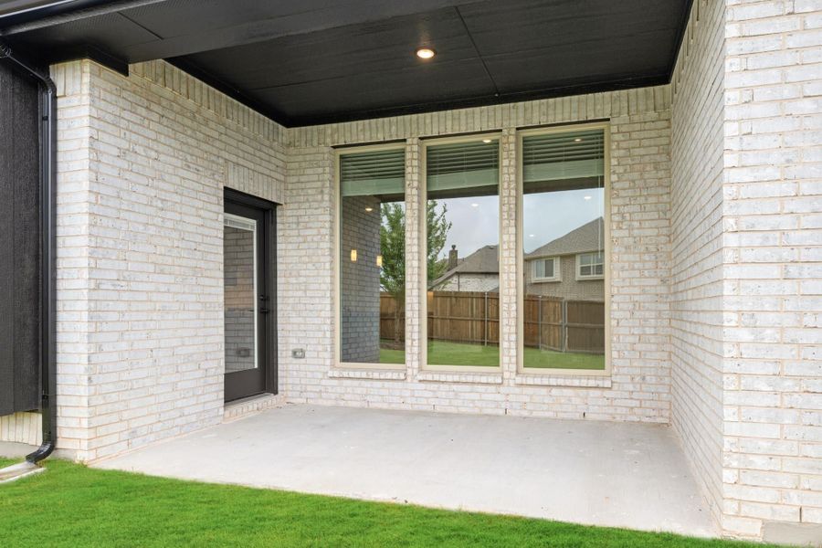 Covered back patio with concrete floor, white brick exterior, large windows, and black door Covered back patio with concrete floor, white brick exterior, large windows, and black door