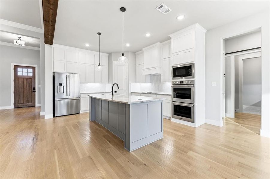 Kitchen featuring appliances with stainless steel finishes, white cabinets, decorative light fixtures, an island with sink, and recessed lighting