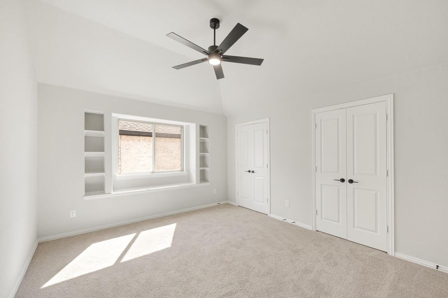 Empty bedroom with vaulted ceiling, ceiling fan, built-in shelves, and double closet doors