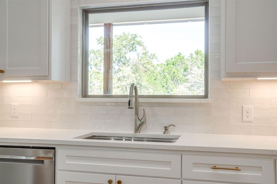 Kitchen featuring tasteful backsplash, stainless steel dishwasher, light stone countertops, and white cabinets Kitchen featuring tasteful backsplash, stainless steel dishwasher, light stone countertops, and white cabinets