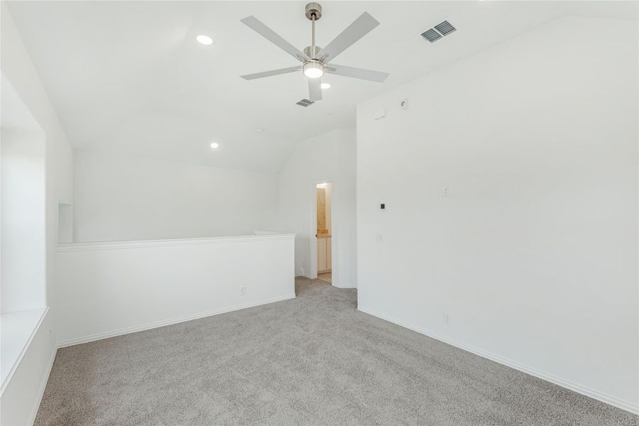 Empty bedroom with vaulted ceiling, ceiling fan, gray carpet, and doorway to bathroom Empty bedroom with vaulted ceiling, ceiling fan, gray carpet, and doorway to bathroom