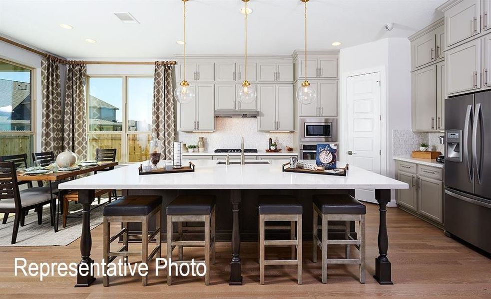 Kitchen featuring hardwood / wood-style floors, backsplash, gray cabinetry, stainless steel appliances, and a center island with sink