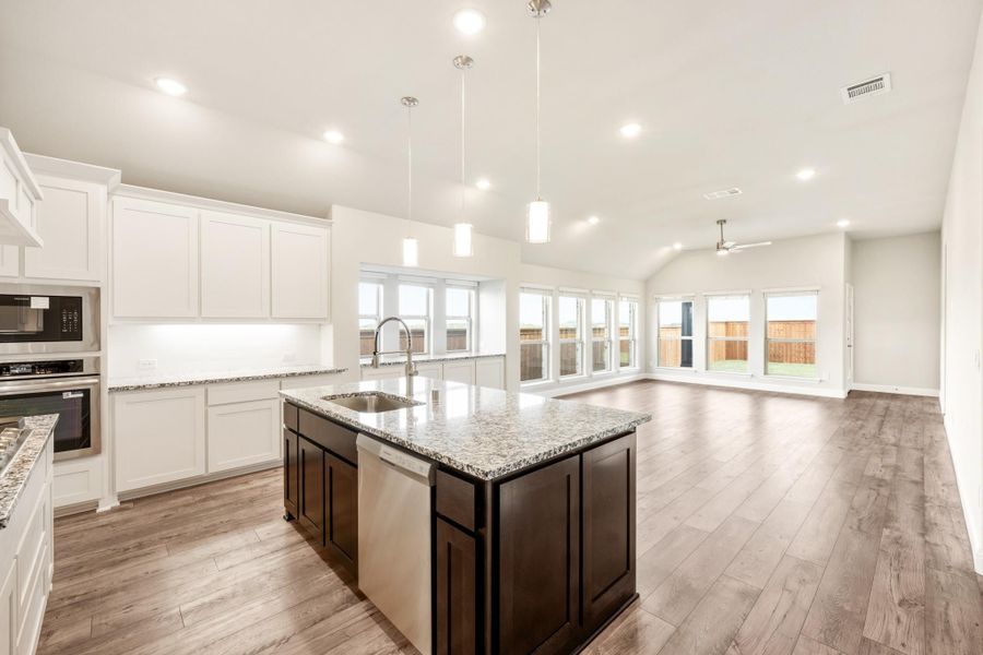 Open kitchen with dark island, granite countertops, white cabinets, and hardwood floors open to living area Open kitchen with dark island, granite countertops, white cabinets, and hardwood floors open to living area