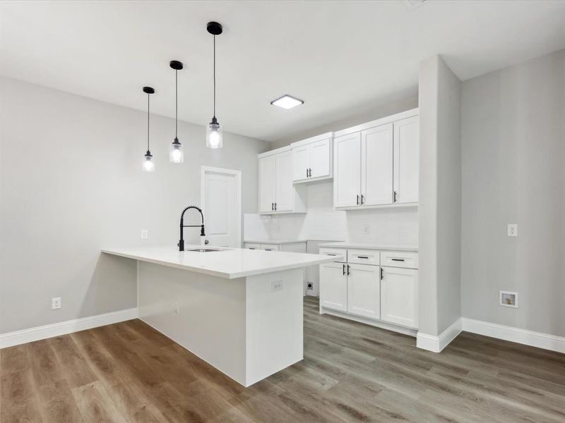 Kitchen with kitchen peninsula, decorative light fixtures, sink, hardwood / wood-style flooring, and white cabinetry