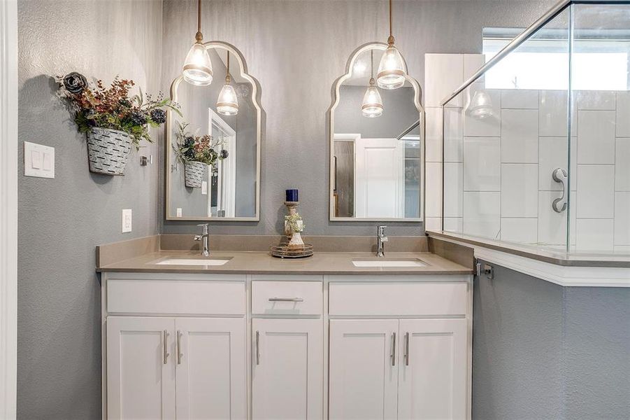 Bathroom featuring a textured wall, tiled shower, a sink, and double vanity