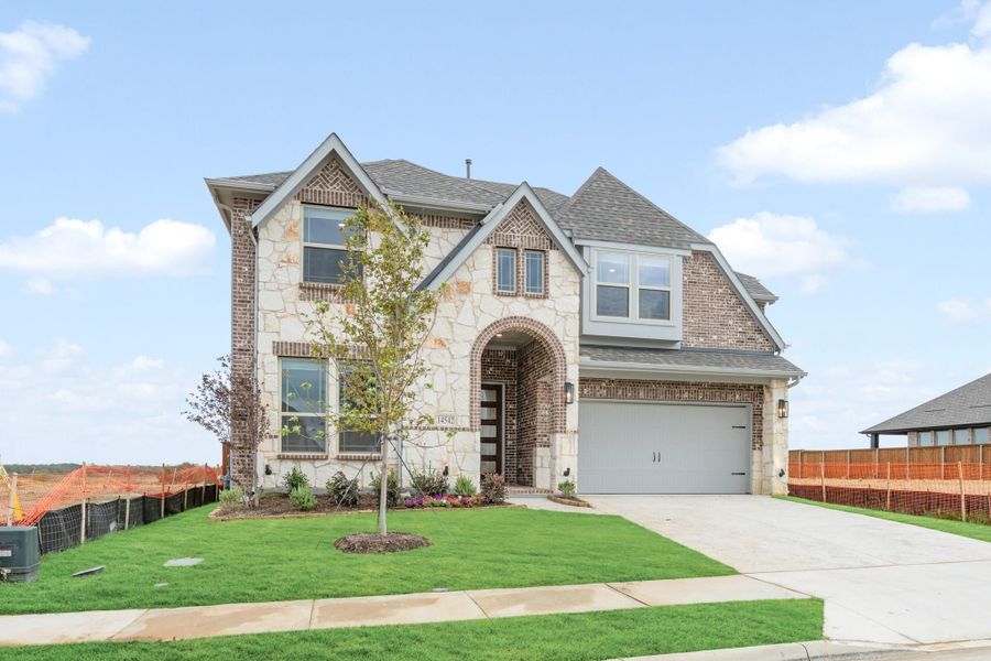 Two-story home with stone and brick exterior, arched entry, two-car garage, and manicured front lawn