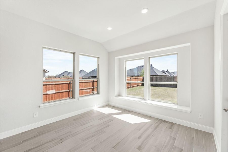 Empty room with light wood-look floors, white walls, and four large windows overlooking a fenced backyard Empty room with light wood-look floors, white walls, and four large windows overlooking a fenced backyard