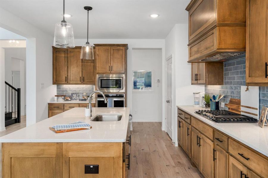 Kitchen featuring tasteful backsplash, appliances with stainless steel finishes, sink, light wood-type flooring, and a kitchen island with sink