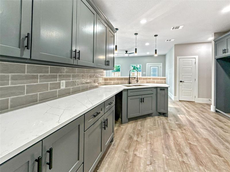 Kitchen featuring tasteful backsplash, gray cabinetry, light wood-type flooring, light stone countertops, and recessed lighting
