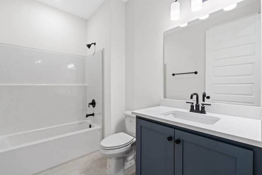 Modern bathroom featuring a dark blue vanity, white countertop with an integrated sink, matte black fixtures, and a white tub with shower surround Modern bathroom featuring a dark blue vanity, white countertop with an integrated sink, matte black fixtures, and a white tub with shower surround