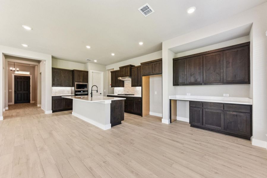 Kitchen featuring tasteful backsplash, dark brown cabinets, recessed lighting, a center island with sink, and light wood-style floors