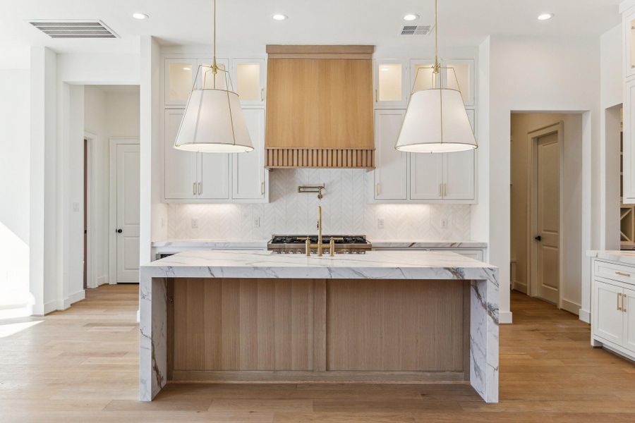 Kitchen features large island with natural white oak finish and waterfall countertops, farmhouse sink, plentiful storage, glass upper cabinets with down lights  *photos are of a previously constructed home by the builder. 1248 Chamboard may have different selections at builders sole discretion. These photos are not meant to be an exact representation of 1248 Chamboard.