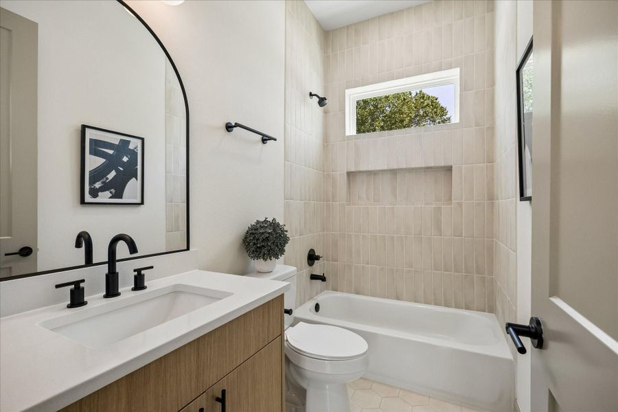 Designer finishes continue with quartz countertops, matte black fixtures, floor to ceiling tile, and an arched mirror that adds warmth and character. Designer finishes continue with quartz countertops, matte black fixtures, floor to ceiling tile, and an arched mirror that adds warmth and character.