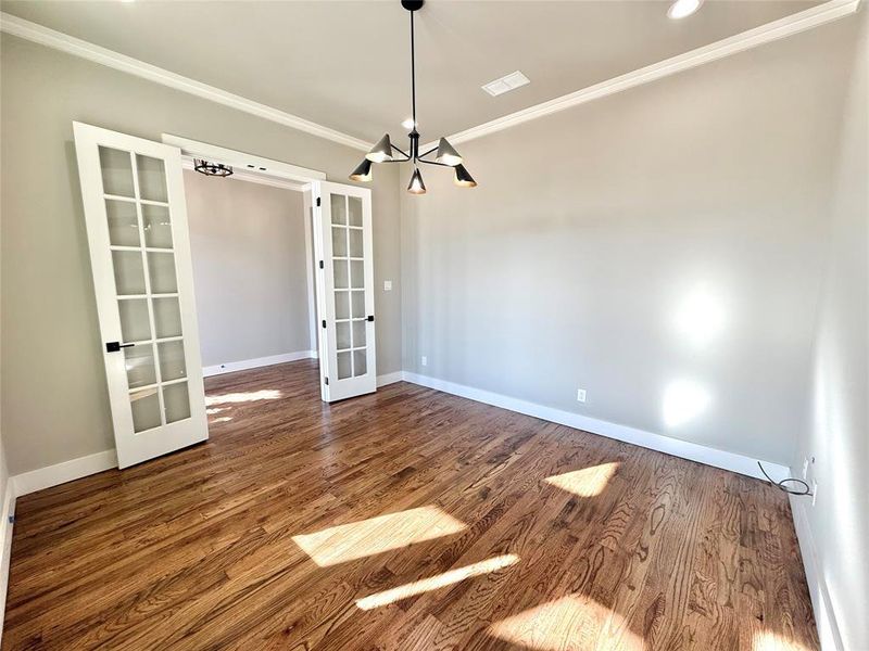 Empty room featuring french doors, a chandelier, ornamental molding, and dark wood-type flooring Empty room featuring french doors, a chandelier, ornamental molding, and dark wood-type flooring