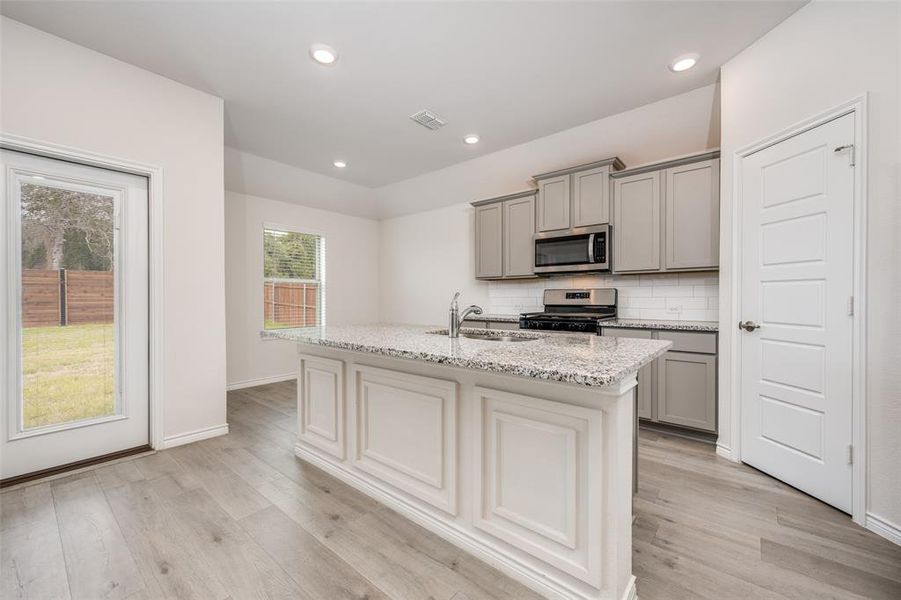 Kitchen with backsplash, light stone countertops, gray cabinets, stainless steel appliances, and recessed lighting