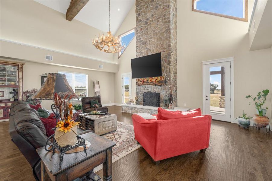 Living room featuring dark wood-style flooring, a stone fireplace, a chandelier, high vaulted ceiling, and beamed ceiling