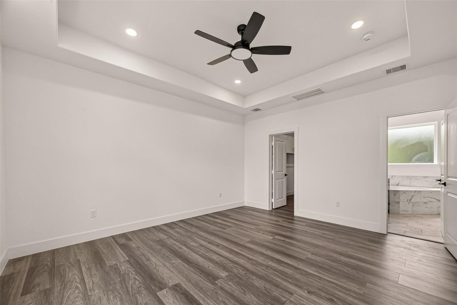 This spacious bedroom features sleek wood flooring, a stylish ceiling fan, and recessed lighting. It connects to a modern bathroom with marble accents, offering a luxurious feel. This spacious bedroom features sleek wood flooring, a stylish ceiling fan, and recessed lighting. It connects to a modern bathroom with marble accents, offering a luxurious feel.