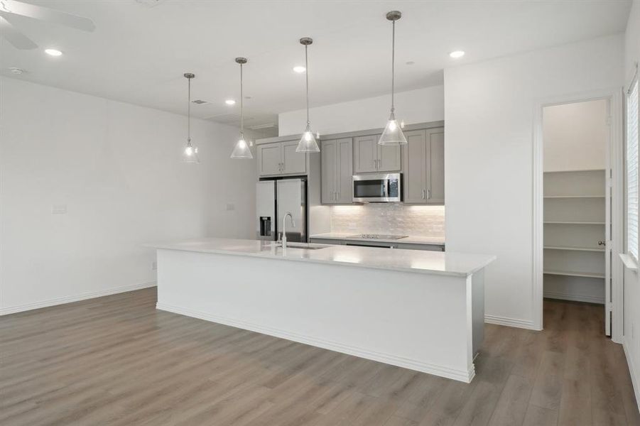 Kitchen with sink, hanging light fixtures, gray cabinets, an island with sink, and stainless steel appliances