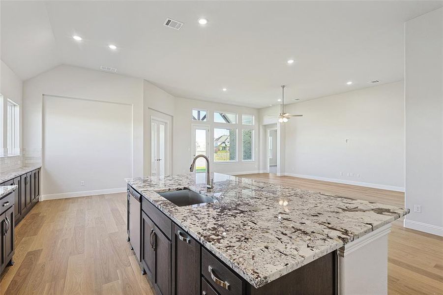 Kitchen with sink, ceiling fan, light stone countertops, an island with sink, and light hardwood / wood-style floors