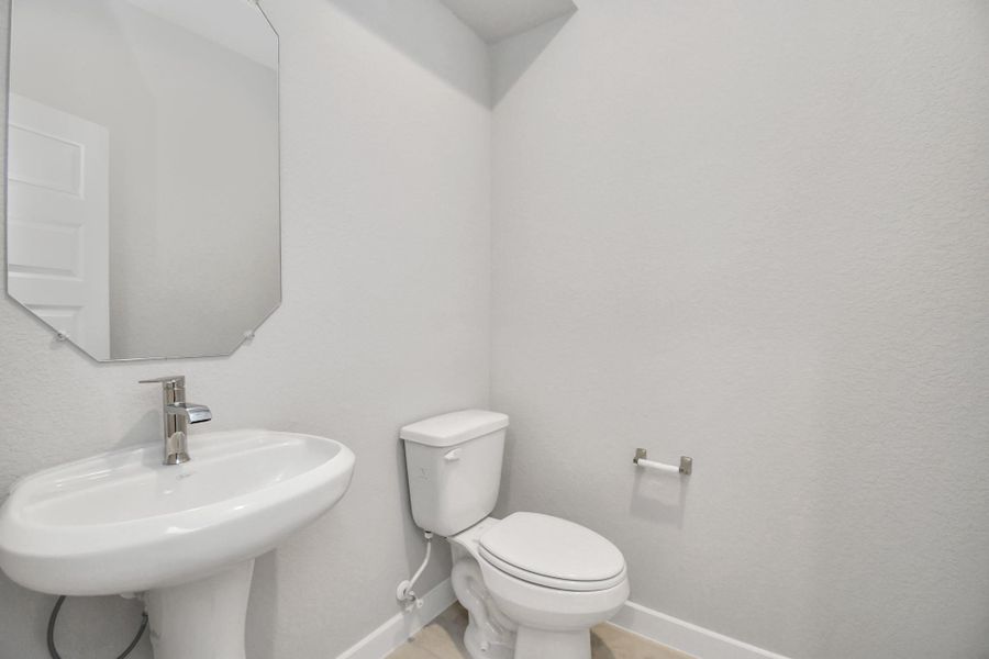 This half bathroom features a stylish pedestal sink, modern hardware, and bright recessed lighting, creating a sleek and inviting space. Sample photo of completed home with similar floor plan. Actual colors and selections may vary.