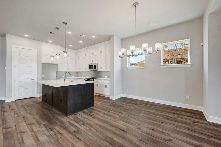 Kitchen featuring a kitchen island with sink, a chandelier, dual tone cabinetry, stainless steel appliances, and dark wood-style floors