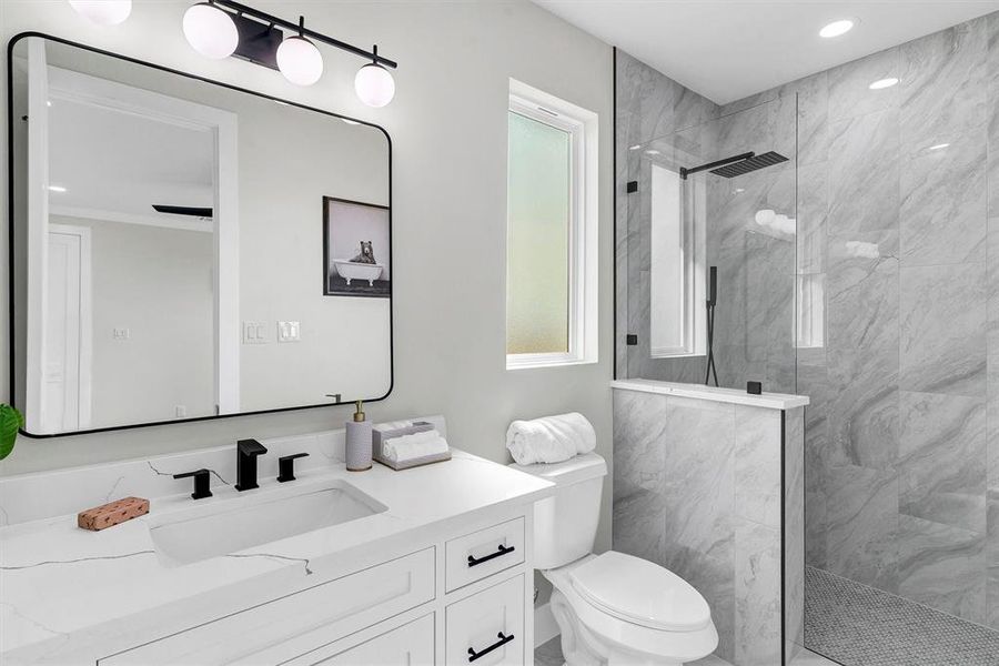 Bathroom featuring toilet, vanity, and tiled shower