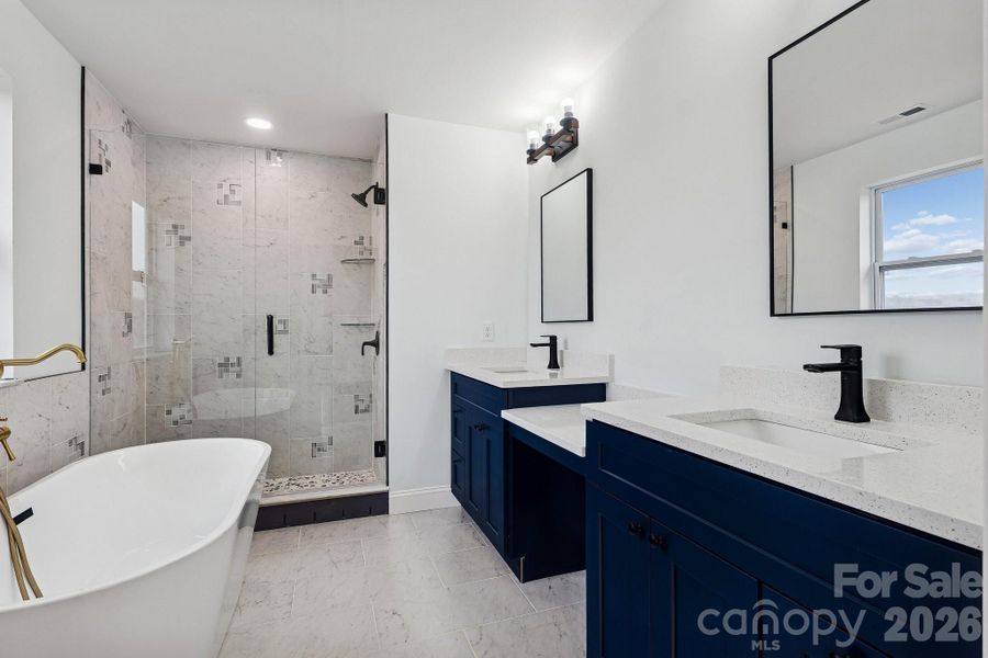 Primary bedroom bathroom suite with his and hers sinks, makeup bar, soaking tub and tile walk-in shower