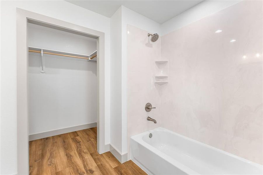 Bathroom with tub / shower combination, wood finished floors, a spacious closet, and baseboards Bathroom with tub / shower combination, wood finished floors, a spacious closet, and baseboards
