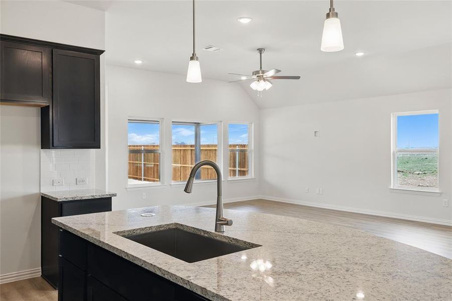 Kitchen featuring light wood-type flooring, light stone counters, decorative light fixtures, dark cabinetry, and vaulted ceiling