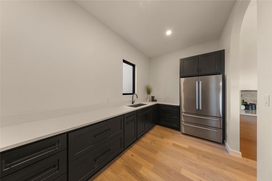 Kitchen with high end refrigerator, light wood-type flooring, dark cabinets, recessed lighting, and light stone countertops