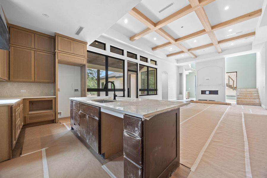 Expansive kitchen and living area featuring a large center island with integrated sink, light wood-tone cabinetry, and a coffered ceiling with recessed lighting
