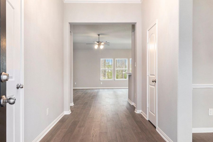 Bright and inviting hallway with light gray walls and wood flooring, leading to a spacious room with large windows and a ceiling fan.
