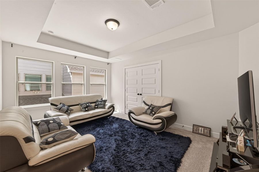 This gameroom features modern furniture with a sleek black and cream color scheme. It has ample natural light from three large windows, a plush dark rug, and a stylish recessed ceiling. Perfect for relaxation or entertaining.