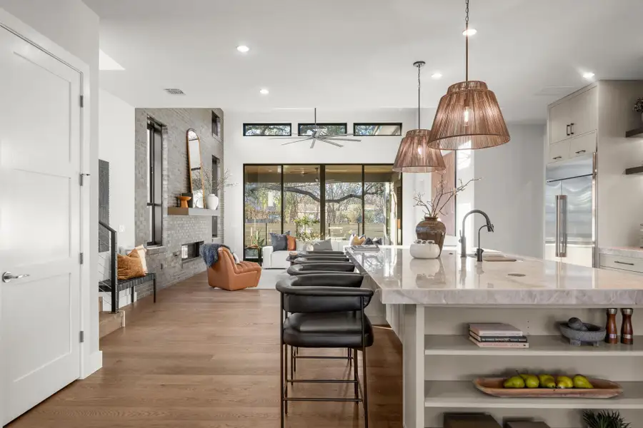 Kitchen with open shelves, light stone counters, light wood finished floors, hanging light fixtures, and ceiling fan