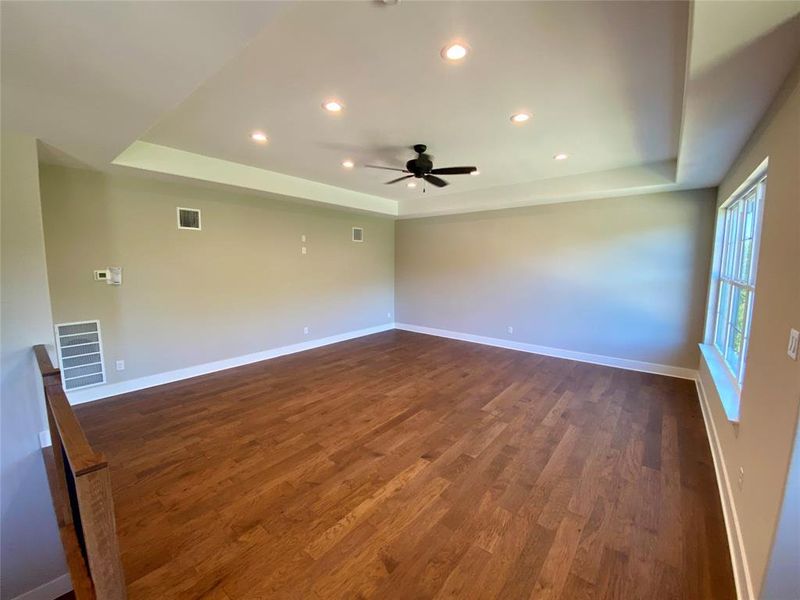 Spare room featuring dark hardwood / wood-style flooring, ceiling fan, and a raised ceiling