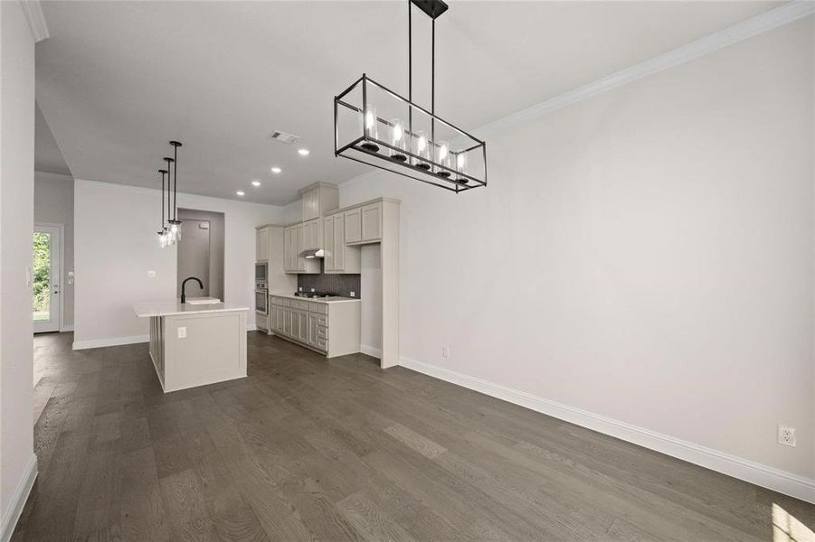 Kitchen featuring dark hardwood / wood-style floors, sink, an island with sink, hanging light fixtures, and crown molding