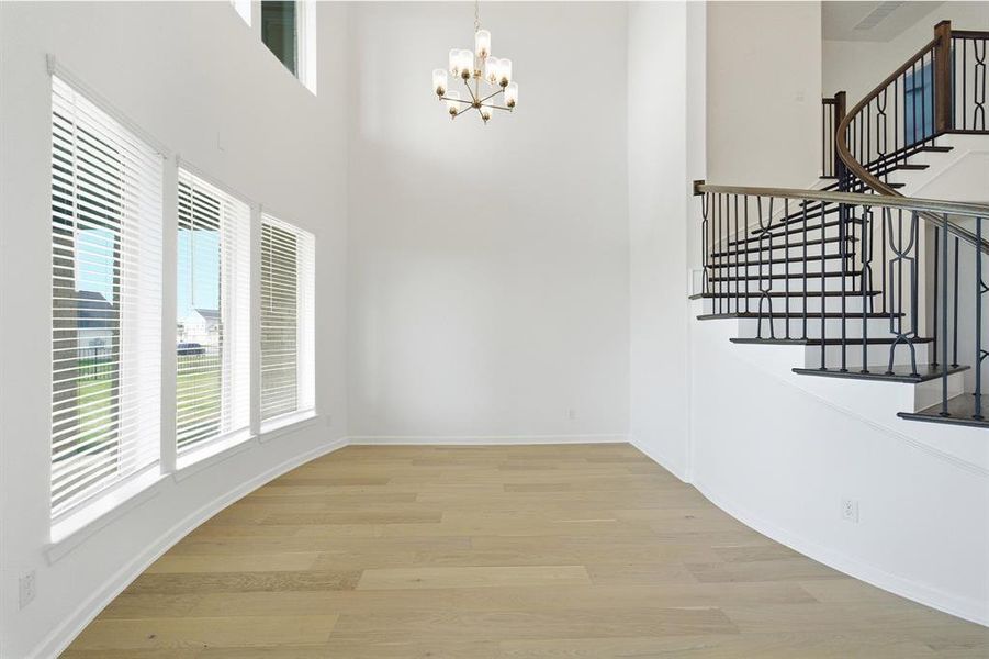 Two-story foyer featuring a curved staircase with wrought iron balusters and wood handrails, wood-finish flooring, a contemporary chandelier, and multiple windows with blinds