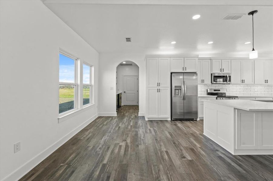 Kitchen with appliances with stainless steel finishes, hanging light fixtures, white cabinets, dark hardwood / wood-style flooring, and decorative backsplash