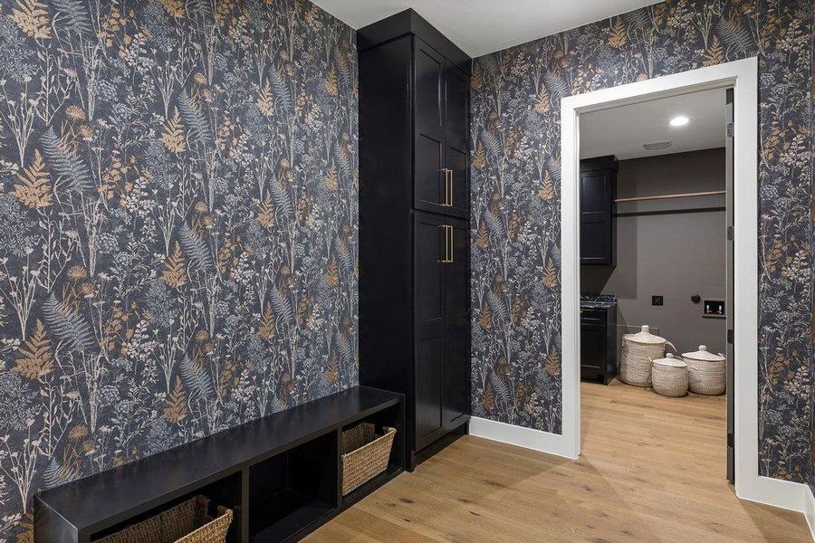 A stylish mudroom with nature-inspired wallpaper leads to a functional laundry area, offering practical storage solutions.