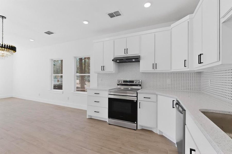 Kitchen with stainless steel appliances, white cabinetry, light wood-style flooring, recessed lighting, and light stone countertops